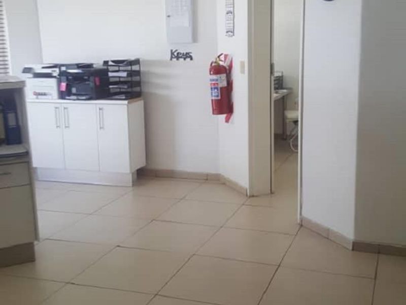 A functional office space featuring tiled flooring, a drop ceiling with integrated lighting, and a wall-mounted fire extinguisher.