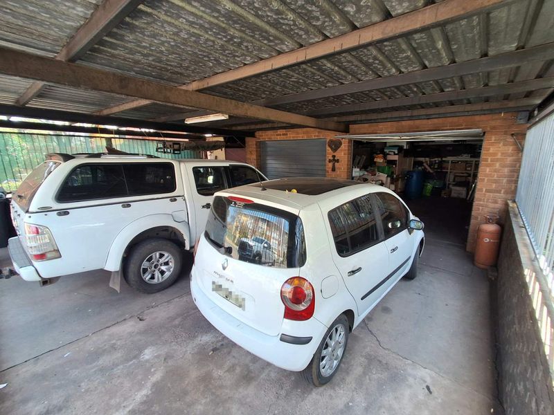 A covered carport and garage area featuring exposed steel beams, corrugated metal roofing, and brick wall construction with concrete flooring.