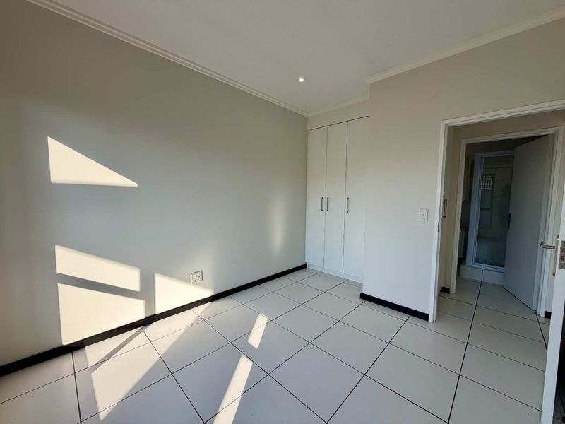 A bright, empty bedroom featuring neutral tiled flooring, built-in cupboards, and clean finishes, offering a versatile space ready for personalization.