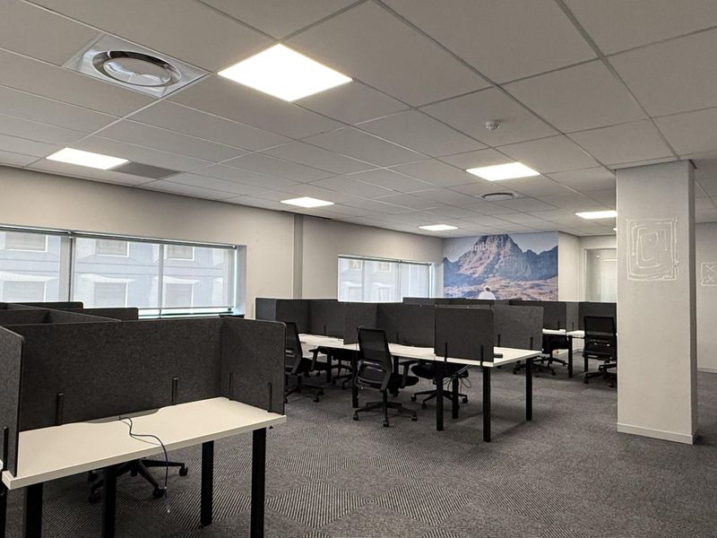 Open-plan office space featuring a suspended ceiling, recessed lighting, carpeted flooring, and large windows providing natural light.