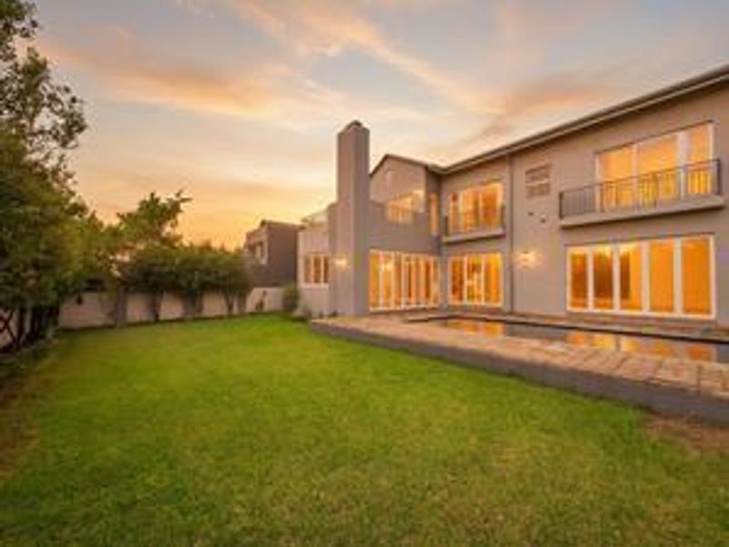 A well-maintained rear exterior view featuring a swimming pool, landscaped garden, and a multi-story home with balconies and large sliding glass doors.