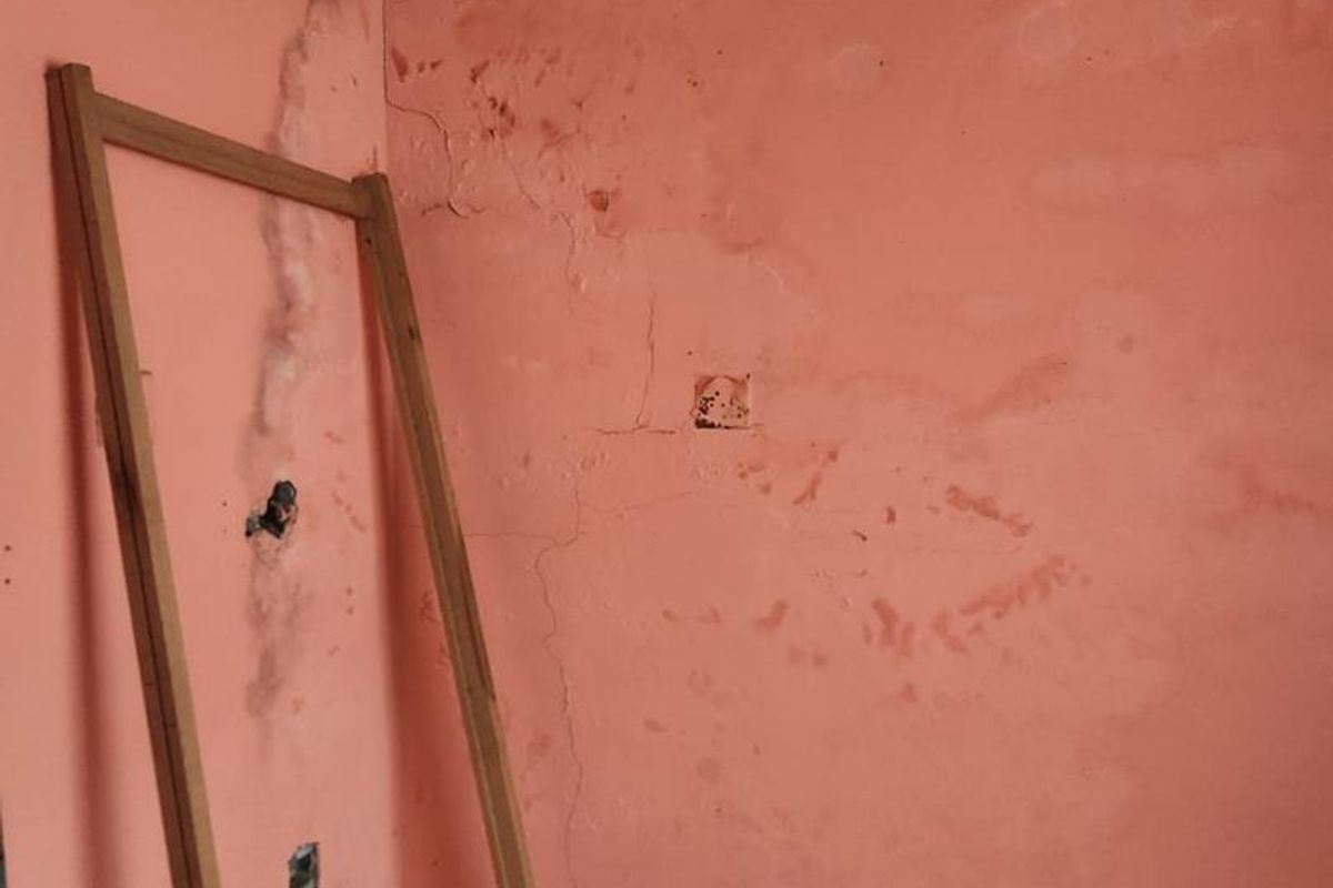 A vacant room featuring significant wall surface deterioration, including visible cracks and peeling paint, requiring extensive repair and refurbishment.