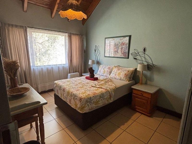 A bedroom featuring a high vaulted timber ceiling, ceramic tiled flooring, and a large window providing natural light.