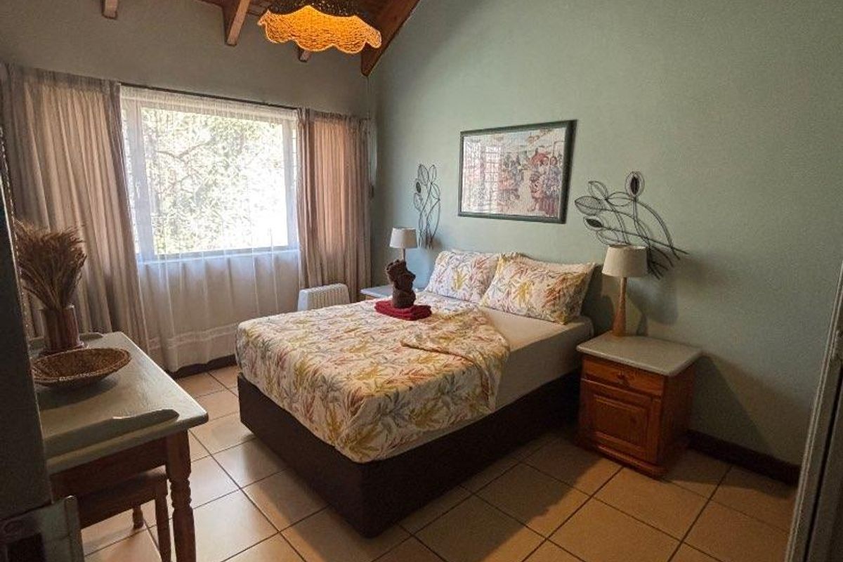 A bedroom featuring a high vaulted timber ceiling, ceramic tiled flooring, and a large window providing natural light.