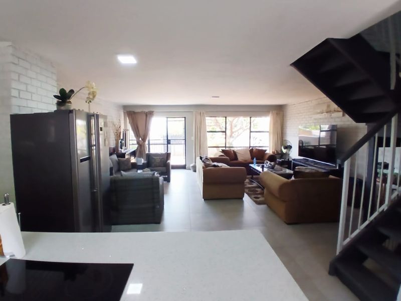 Spacious open-plan living area featuring tiled floors, exposed brick walls, and a staircase, with direct access to an outdoor patio through sliding glass doors.