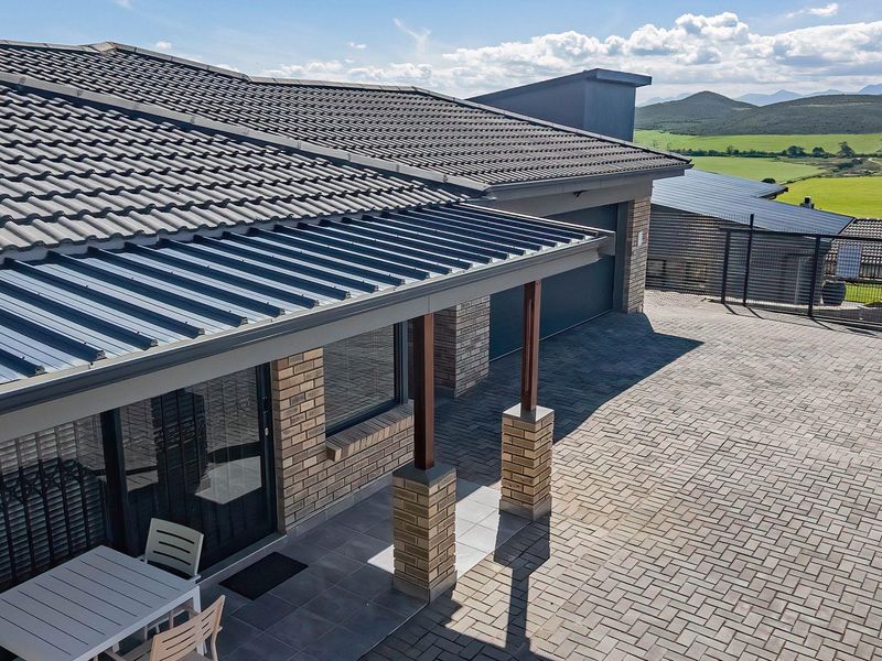 Modern house exterior featuring a paved driveway, covered patio area, brick facade, and a combination of tiled and metal roofing with scenic views.
