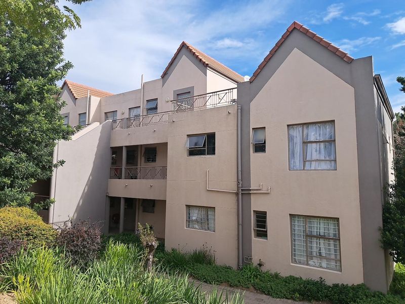 Rear elevation of a multi-story apartment complex featuring terracotta roof tiles, metal balcony railings, and aluminium-framed windows set within landscaped grounds.