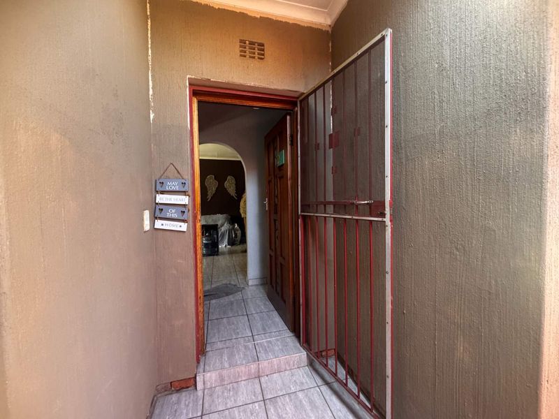 An exterior entrance area featuring a security gate, tiled flooring, and an arched doorway leading into the interior of the home.