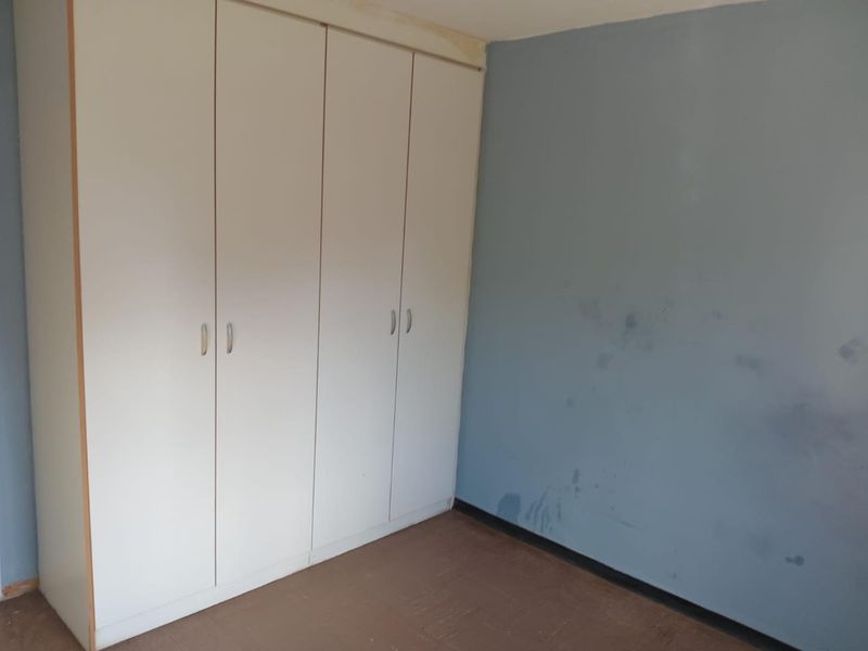 A bedroom featuring built-in cupboards, requiring cosmetic updates to the walls and flooring to improve its overall condition.