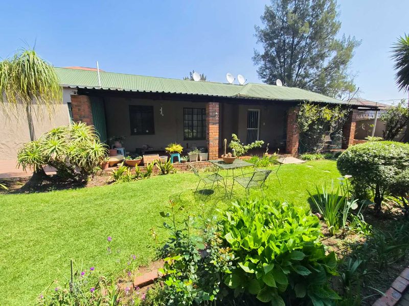 Rear view of the house featuring a covered patio with brick pillars, a corrugated metal roof, and a well-maintained garden area.