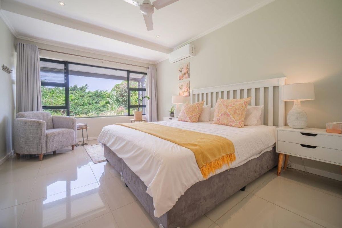A bright and spacious bedroom featuring large windows with garden views, tiled flooring, and a wall-mounted air conditioning unit.