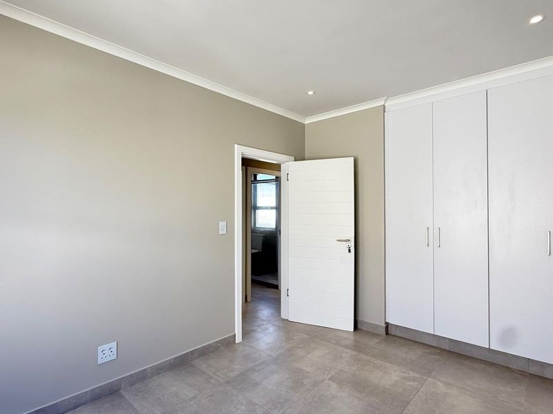 A clean, empty bedroom featuring neutral wall tones, tiled flooring, and ample built-in cupboard storage with modern recessed lighting.