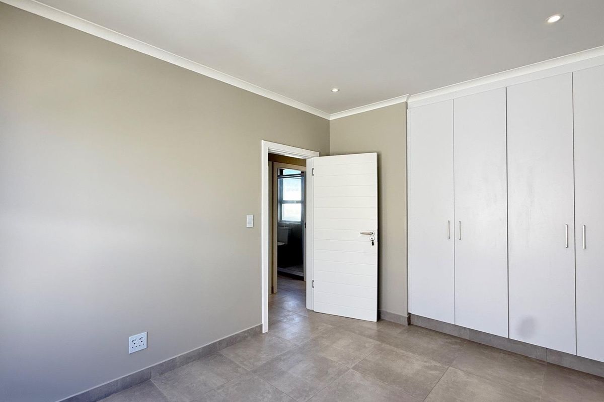 A clean, empty bedroom featuring neutral wall tones, tiled flooring, and ample built-in cupboard storage with modern recessed lighting.
