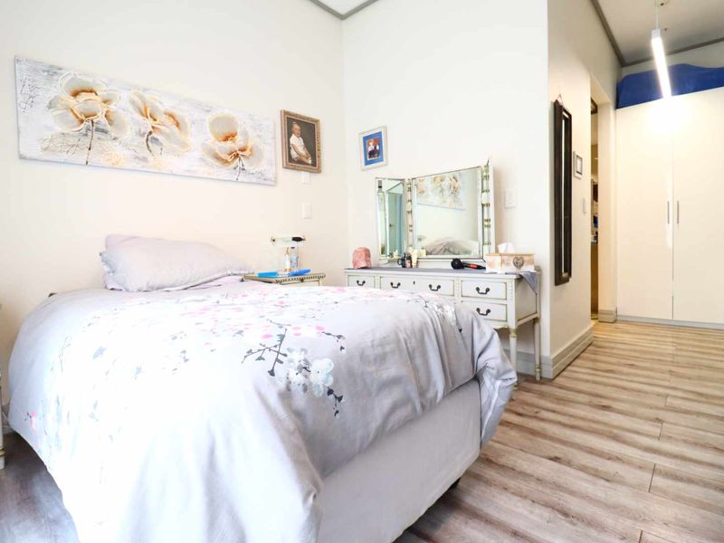 A well-maintained bedroom featuring light-toned laminate flooring, neutral walls, and built-in storage cupboards.