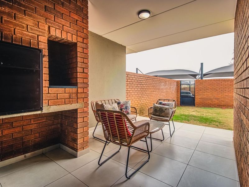 A covered patio featuring a built-in brick braai, tiled flooring, and direct access to a private garden area.
