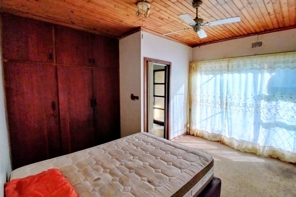 A bedroom featuring built-in wooden cupboards, a timber-clad ceiling with a ceiling fan, and access to an outdoor area via sliding glass doors.