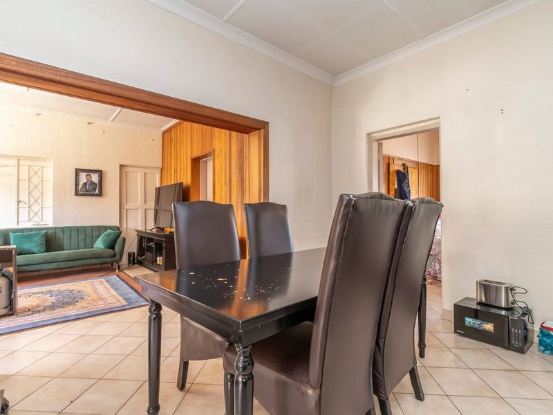 Open plan dining and living area featuring tiled flooring, wood paneling accents, and a connecting doorway between the two living spaces.