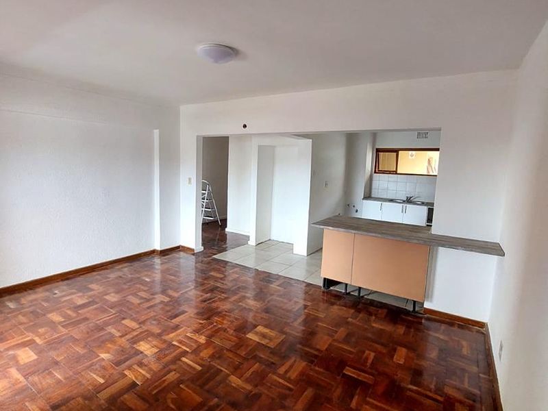 Open plan living area featuring traditional parquet flooring and a breakfast bar connecting to a functional kitchen space.