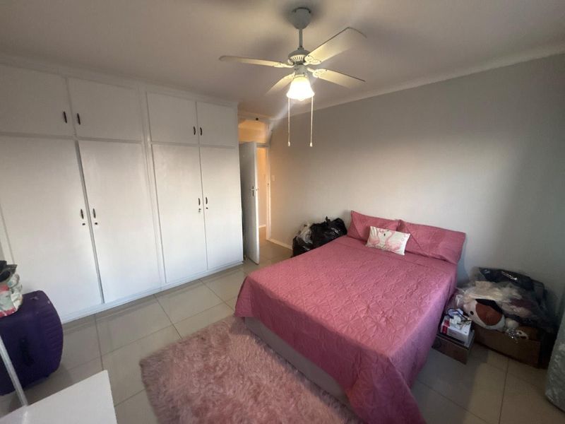 A bedroom featuring built-in cupboards, a ceiling fan, and tiled flooring.