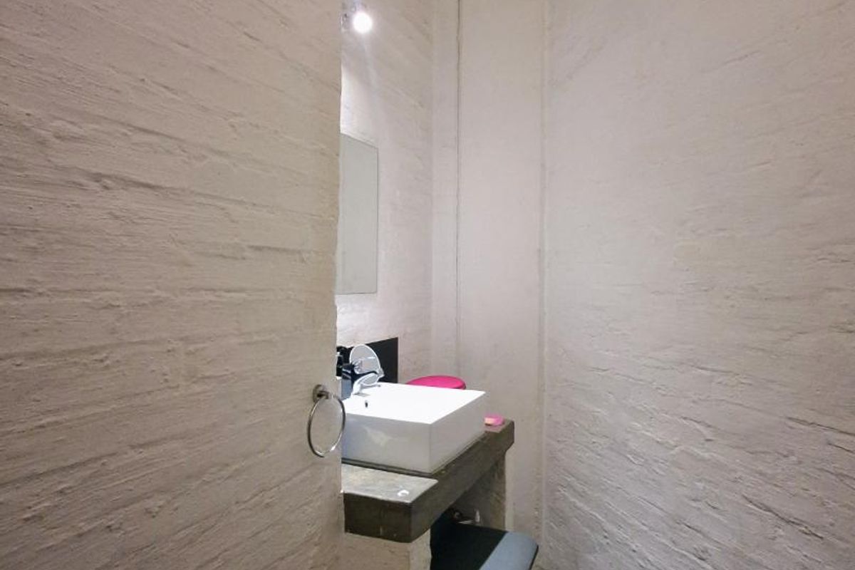 A compact bathroom featuring a vessel sink on a concrete vanity, set against industrial-style exposed white-painted brick walls and an unfinished ceiling.