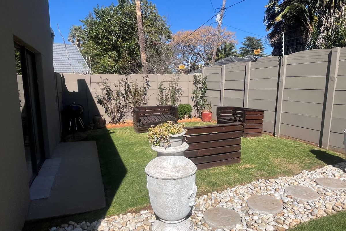 A private rear garden featuring a well-maintained lawn, paved pathway, and secure perimeter walling with electric fencing.