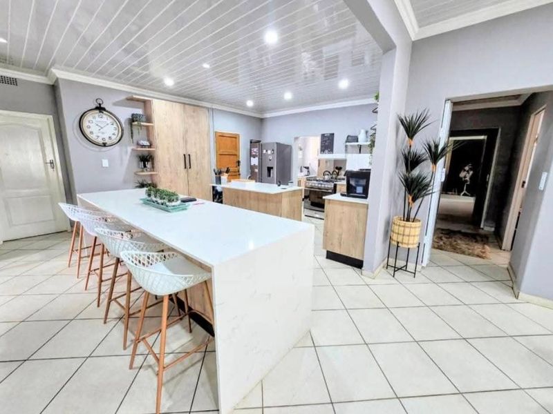 Modern open-plan kitchen featuring a large central island with quartz countertops, sleek cabinetry, recessed lighting, and tiled flooring throughout the space.