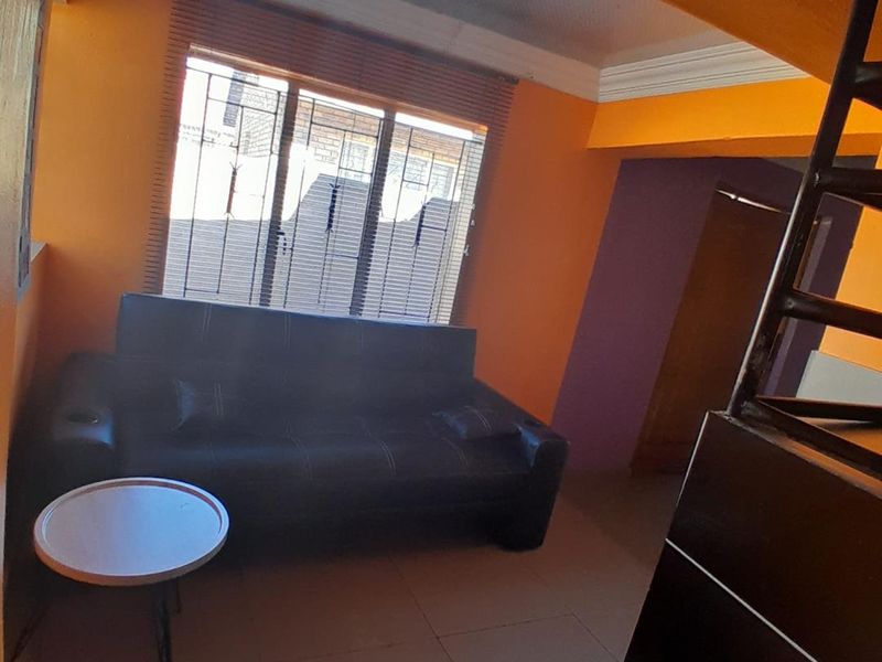 A living area featuring tiled flooring, decorative cornice, and venetian blinds, currently finished with bold orange wall paint.