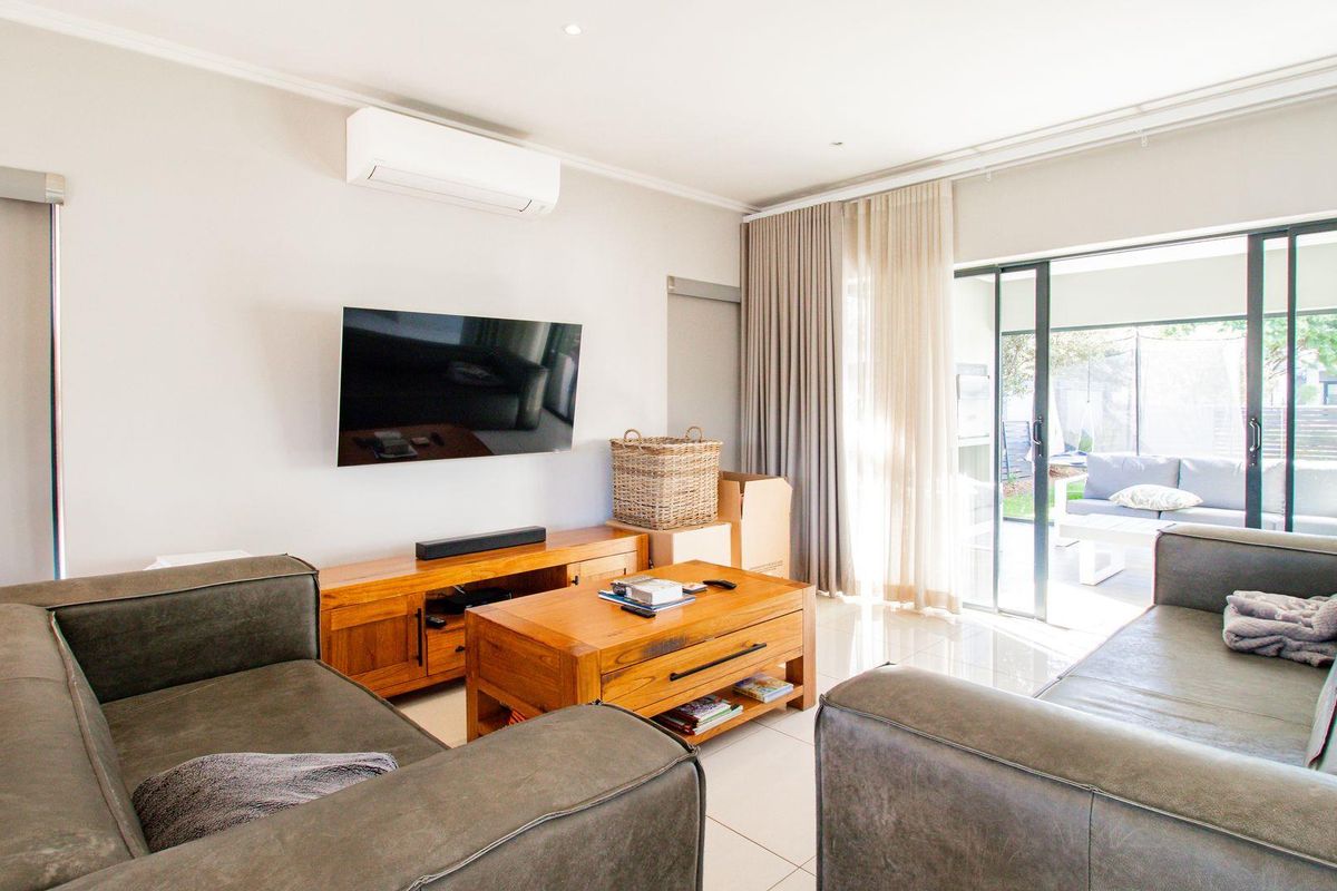A bright and modern living room featuring tiled flooring, a wall-mounted air conditioning unit, and large sliding glass doors leading to an outdoor patio.