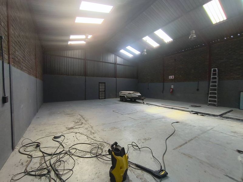 Spacious industrial warehouse unit featuring high ceilings with skylights, exposed brick walls, and durable concrete flooring, suitable for various commercial or storage applications.