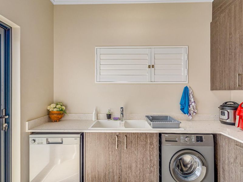 A functional laundry area featuring modern wood-finish cabinetry, stone countertops, a double basin sink, and integrated space for a dishwasher and washing machine.