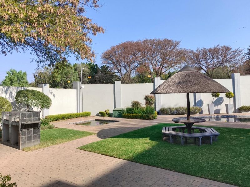 Outdoor entertainment area featuring a swimming pool, built-in braai, and a thatched lapa set within a secure, walled garden.