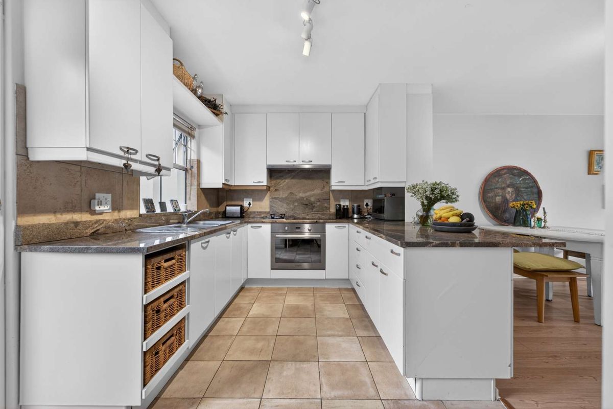 A functional U-shaped kitchen featuring white cabinetry, granite countertops, a stainless steel oven, and tiled flooring with a stone backsplash.