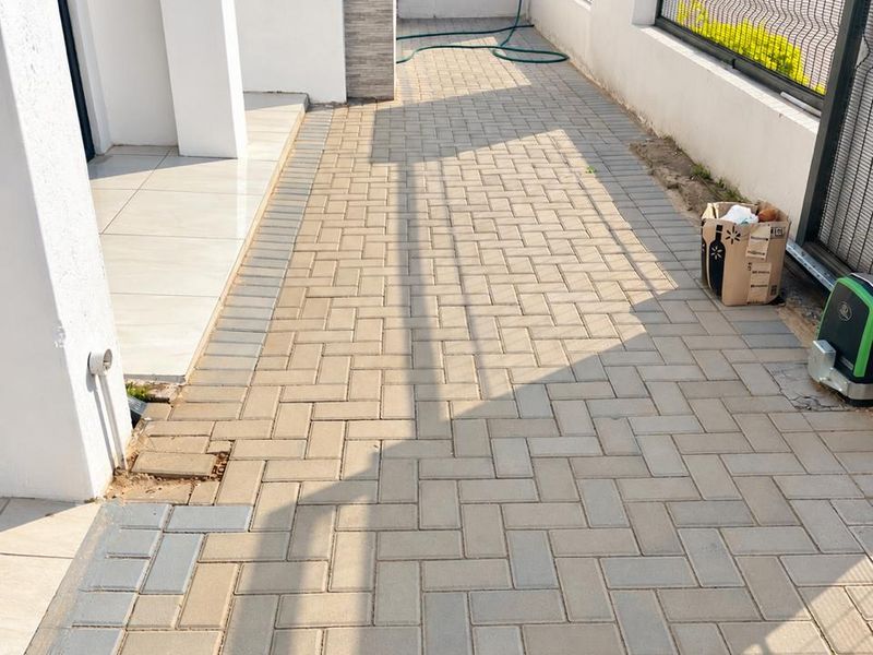 A paved side walkway and patio area featuring a boundary wall with metal fencing and a gate motor installation.