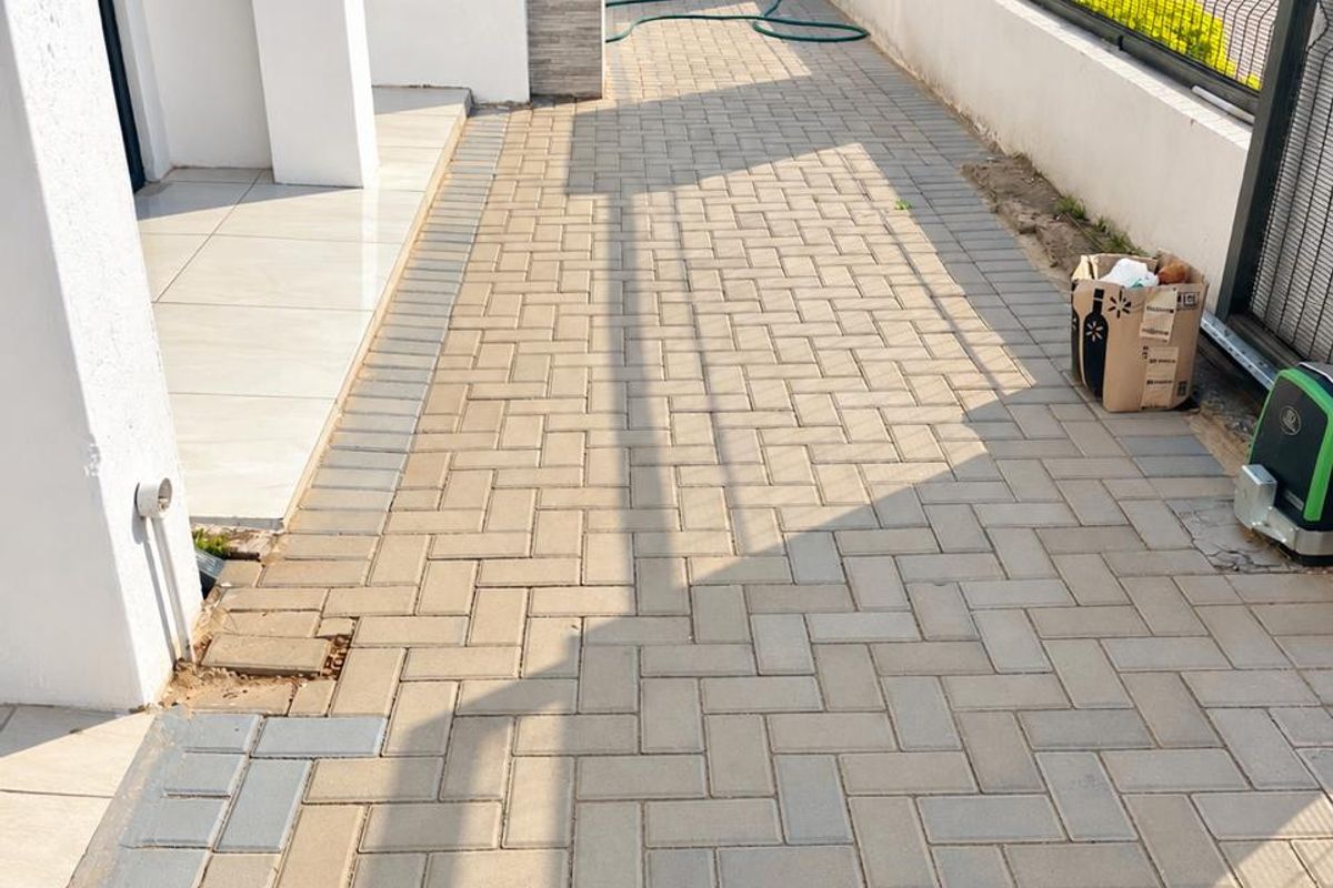 A paved side walkway and patio area featuring a boundary wall with metal fencing and a gate motor installation.