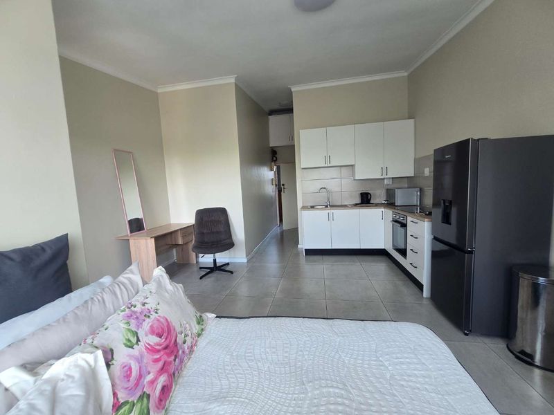 Open-plan studio apartment featuring a compact kitchen with white cabinetry, built-in oven, and tiled flooring throughout the living and sleeping area.
