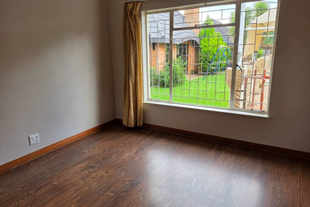 A bright, empty bedroom featuring wood-look laminate flooring, a large window with security bars, and views overlooking the rear garden.