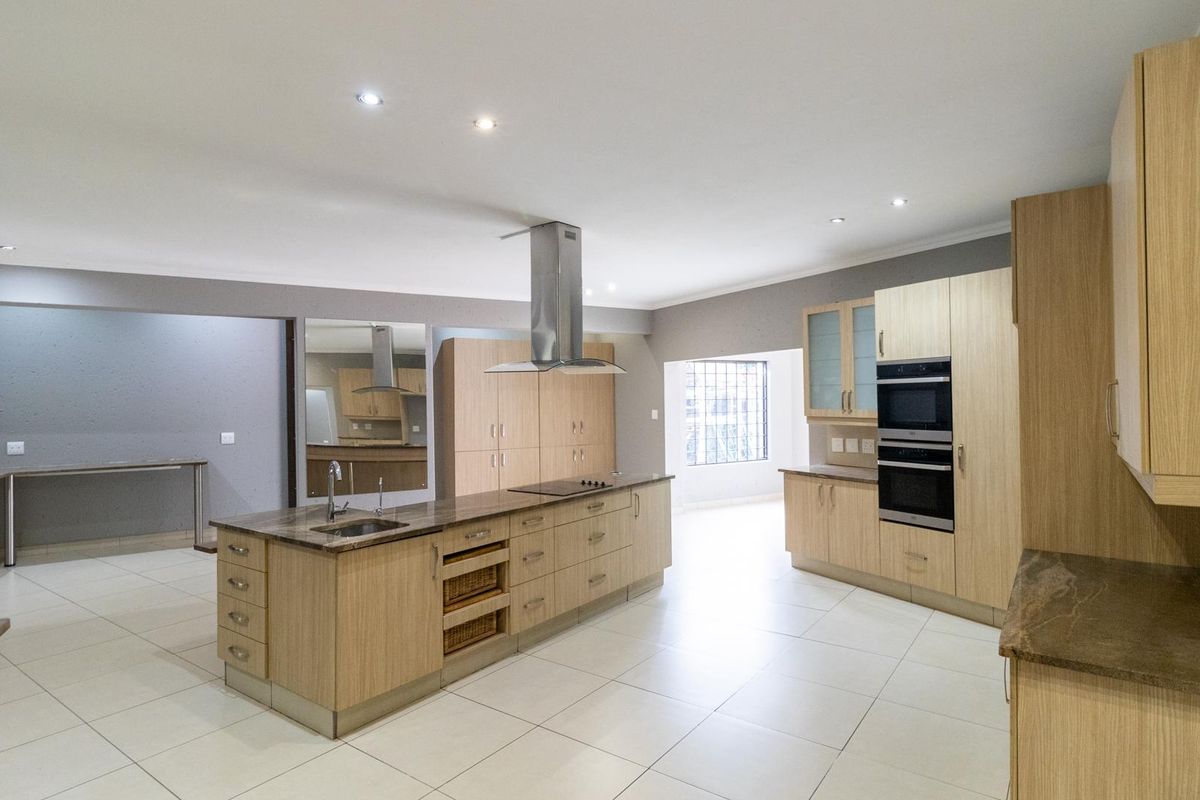 Spacious modern kitchen featuring a large central island with integrated sink, built-in double oven, and sleek light wood cabinetry throughout.