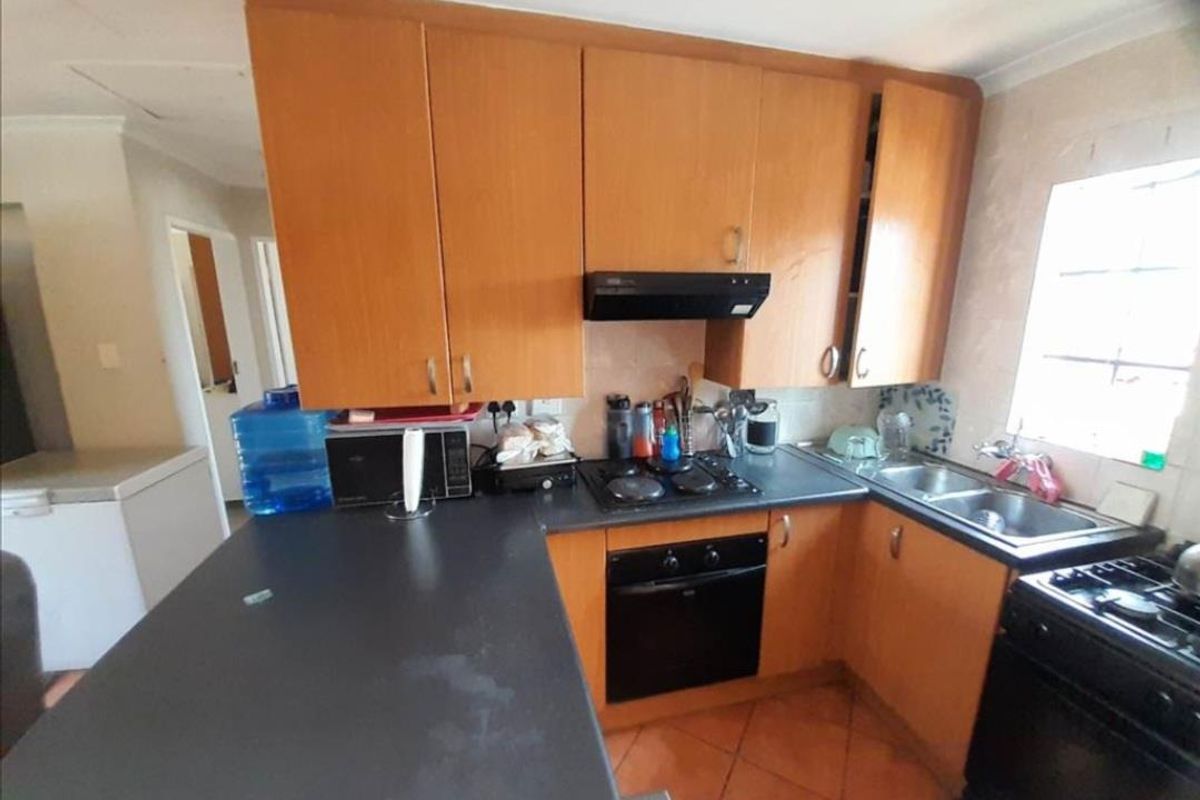 A functional kitchen featuring wood-finish cabinetry, dark laminate countertops, a built-in oven, hob, and extractor fan with tiled flooring.