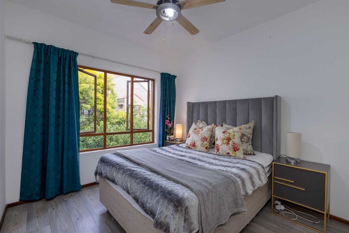 A well-maintained bedroom featuring laminate flooring, a ceiling fan, and a large timber-framed window providing natural light and garden views.