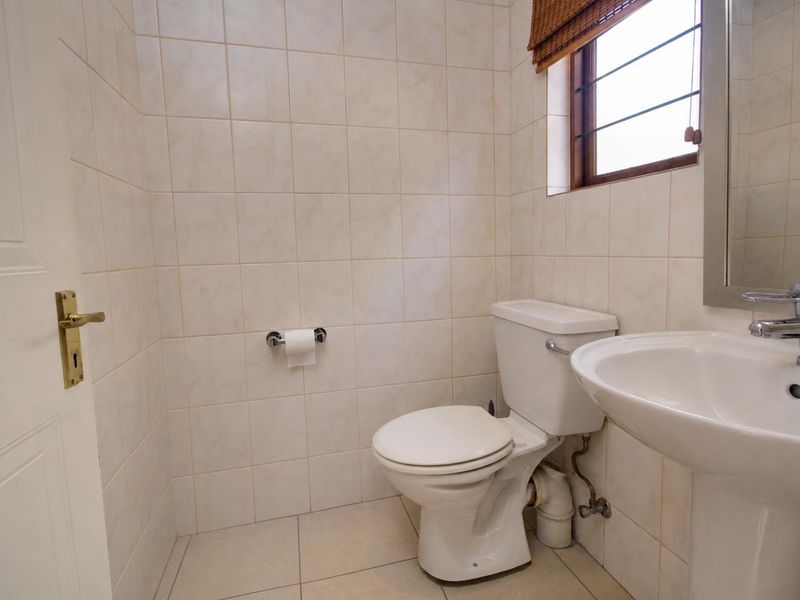 A compact guest bathroom featuring a pedestal basin, toilet, and neutral wall and floor tiling.