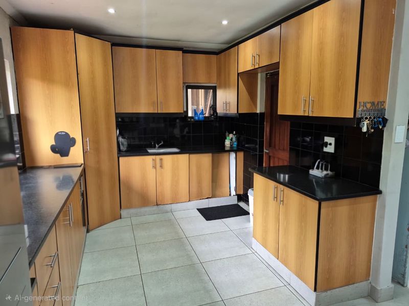 Functional kitchen featuring wood-look laminate cabinetry, black granite countertops, and a tiled backsplash with recessed lighting.