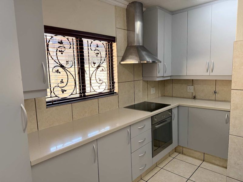 A modern, well-maintained kitchen featuring light grey cabinetry, stone countertops, a built-in oven, electric hob, and a stainless steel extractor fan.