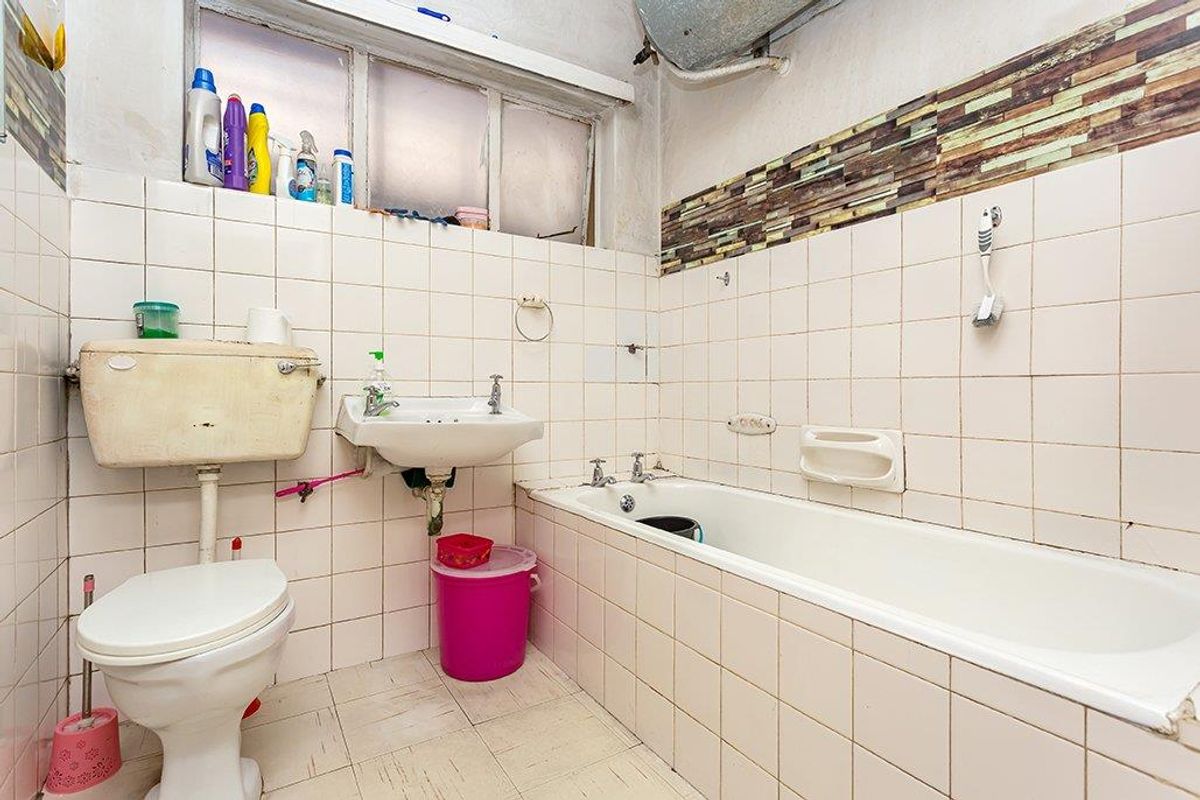 A dated bathroom featuring a built-in bathtub, pedestal basin, and flush toilet, requiring significant renovation and modernization of finishes and fixtures.