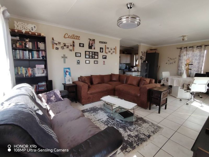 An open-plan living and dining area featuring tiled flooring and a ceiling fan, with an integrated kitchen space visible in the background.