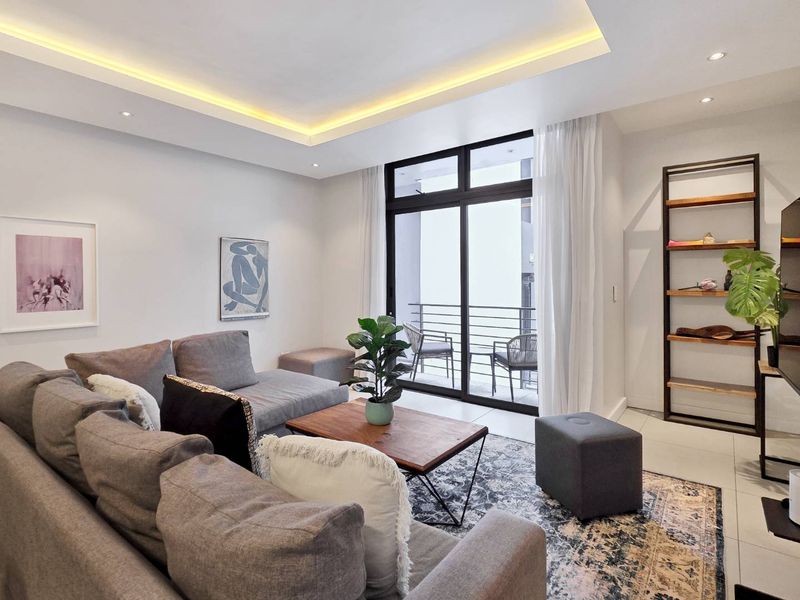 Modern living room featuring recessed cove lighting, tiled floors, and large sliding glass doors providing access to a private balcony.