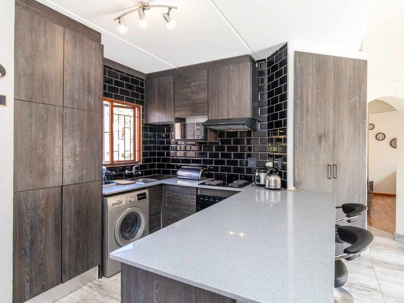 Modern kitchen featuring dark wood cabinetry, stone countertops, a breakfast bar, and a stylish black subway tile backsplash.