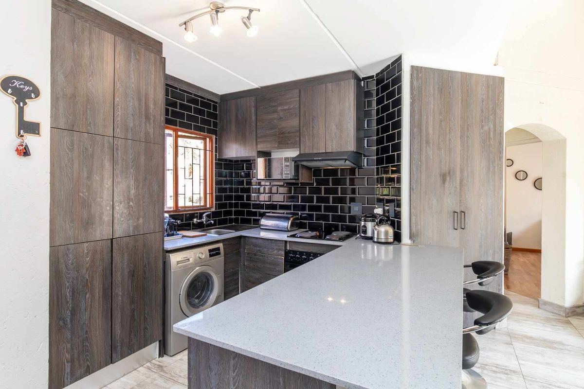 Modern kitchen featuring dark wood cabinetry, stone countertops, a breakfast bar, and a stylish black subway tile backsplash.