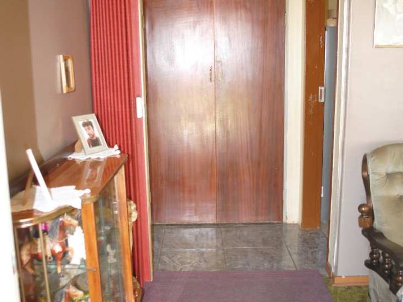 A dated hallway featuring built-in wooden cupboards, a combination of carpet and tile flooring, and a traditional chandelier fixture.