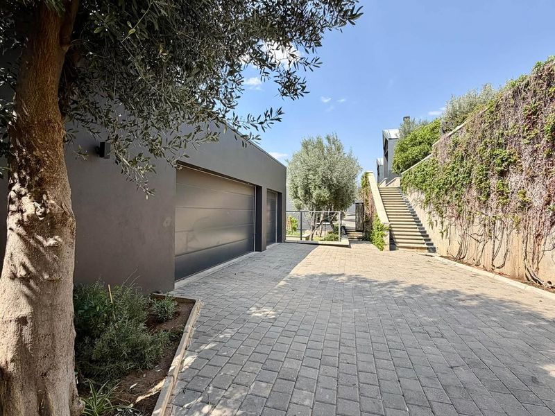 Modern townhouse exterior featuring a double garage, paved driveway, and a concrete staircase leading to the upper level with landscaped retaining walls.