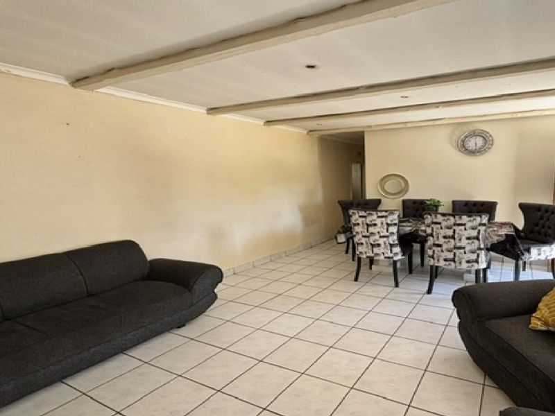 Open-plan living and dining area featuring ceramic floor tiles and exposed ceiling beams, offering a spacious layout for family living.